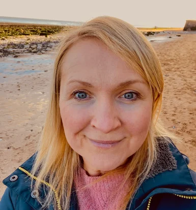 headshotforwebsite Friendly headshot of Zoe outdoors with a seaside sunset in the background.
